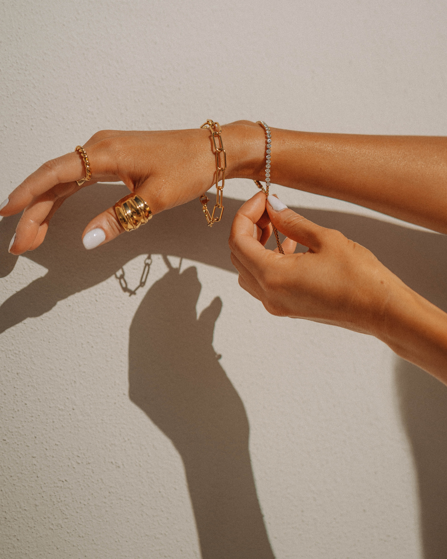 Close-up of a hand wearing gold jewelry on a neutral background- permanent or with a clasp