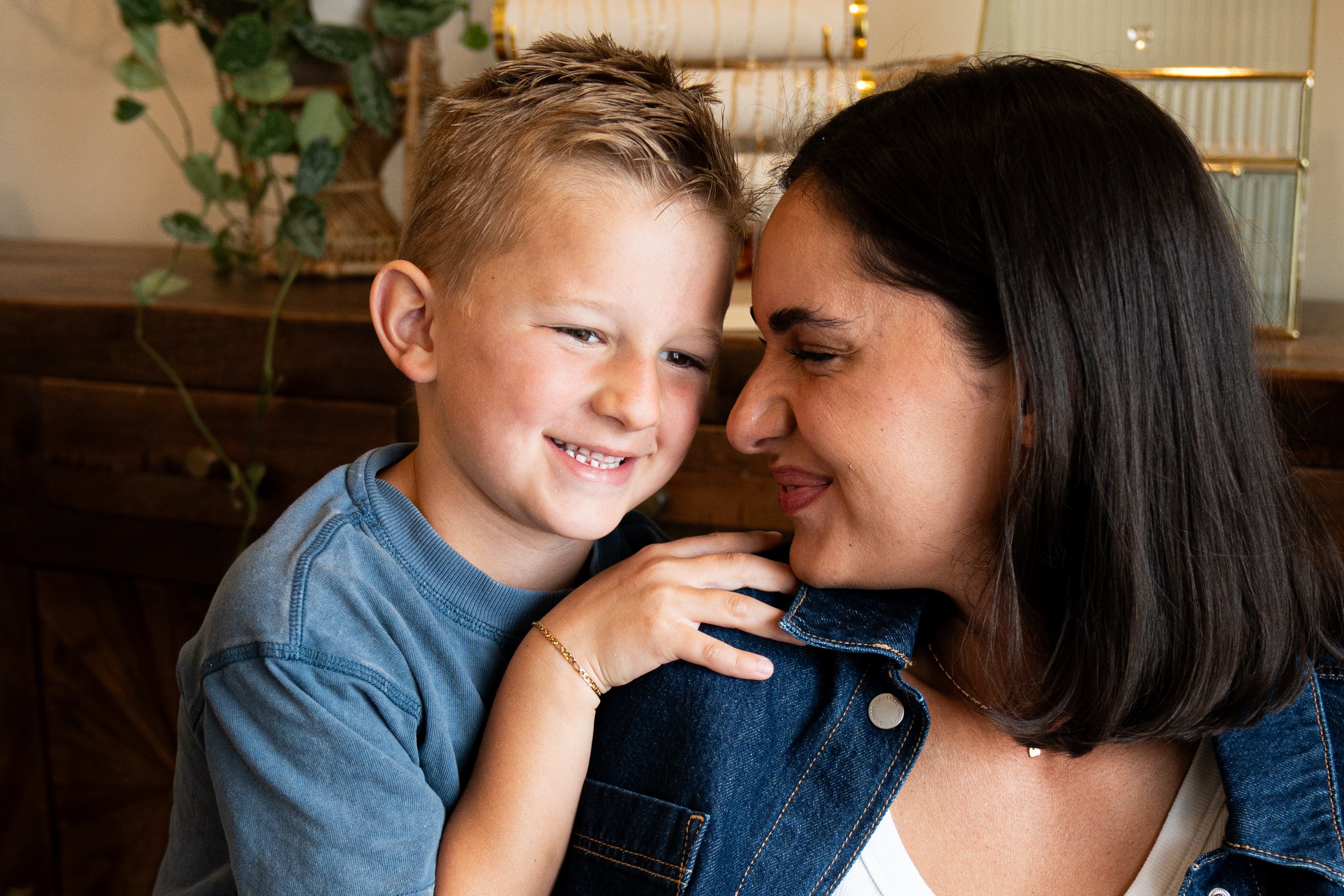 Woman and young boy standing close together indoors, smiling.