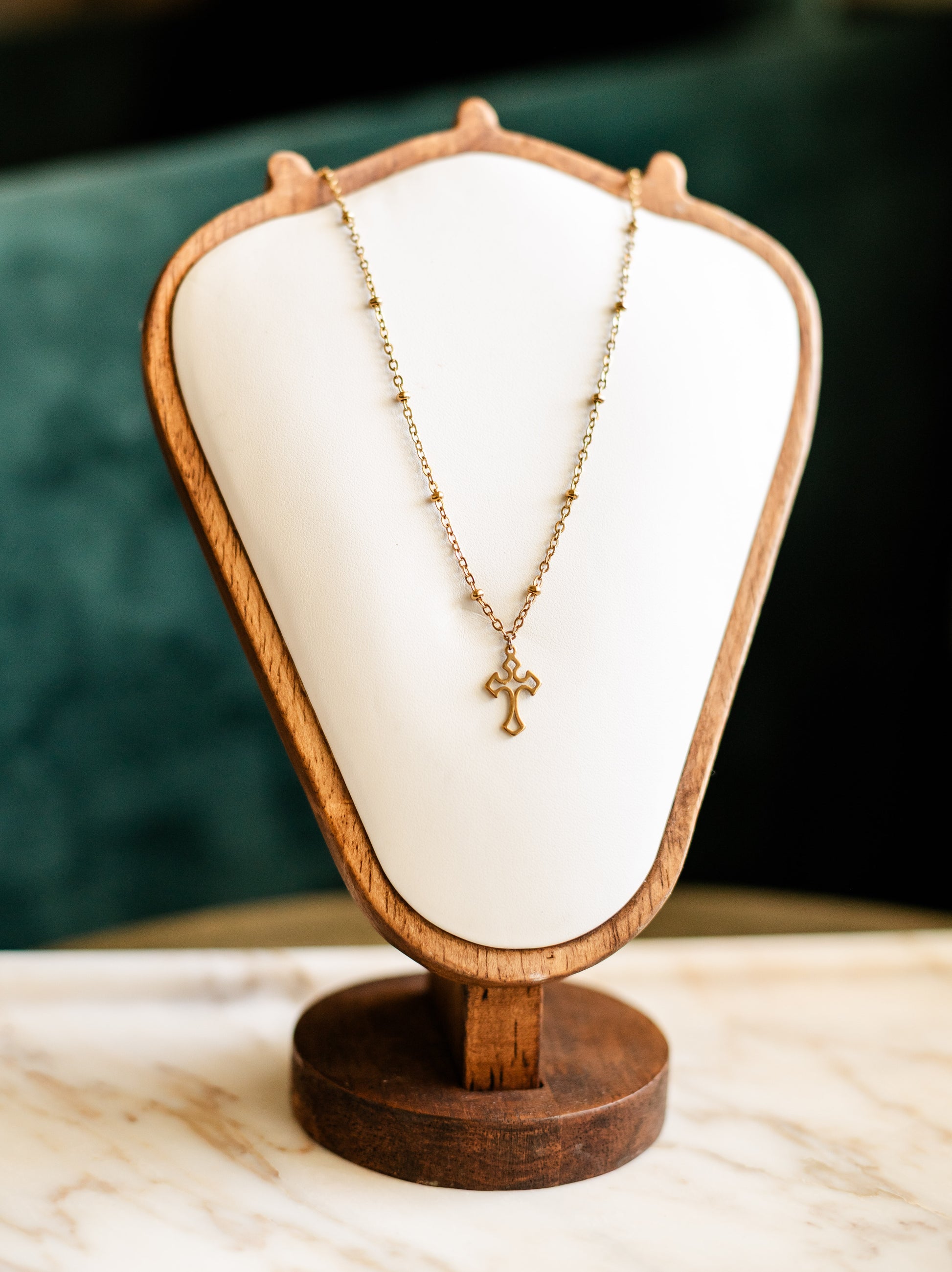 Necklace with a cross pendant on a wooden display stand against a dark background